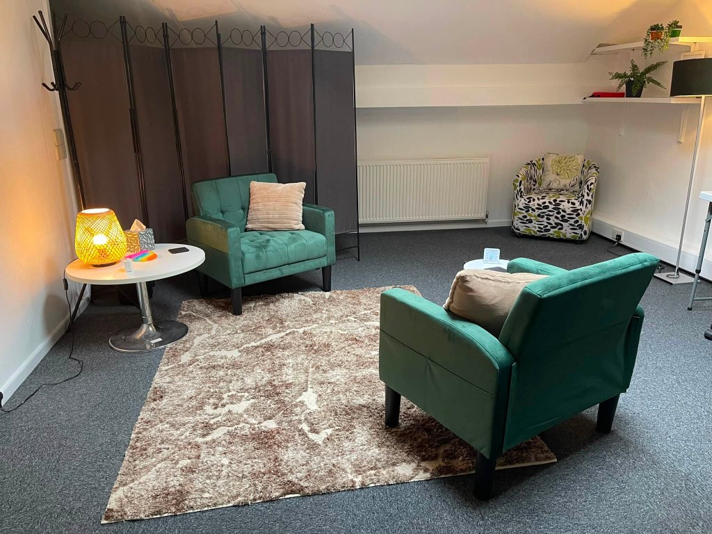 A second counselling room with green armchairs, soft lamp light and plants